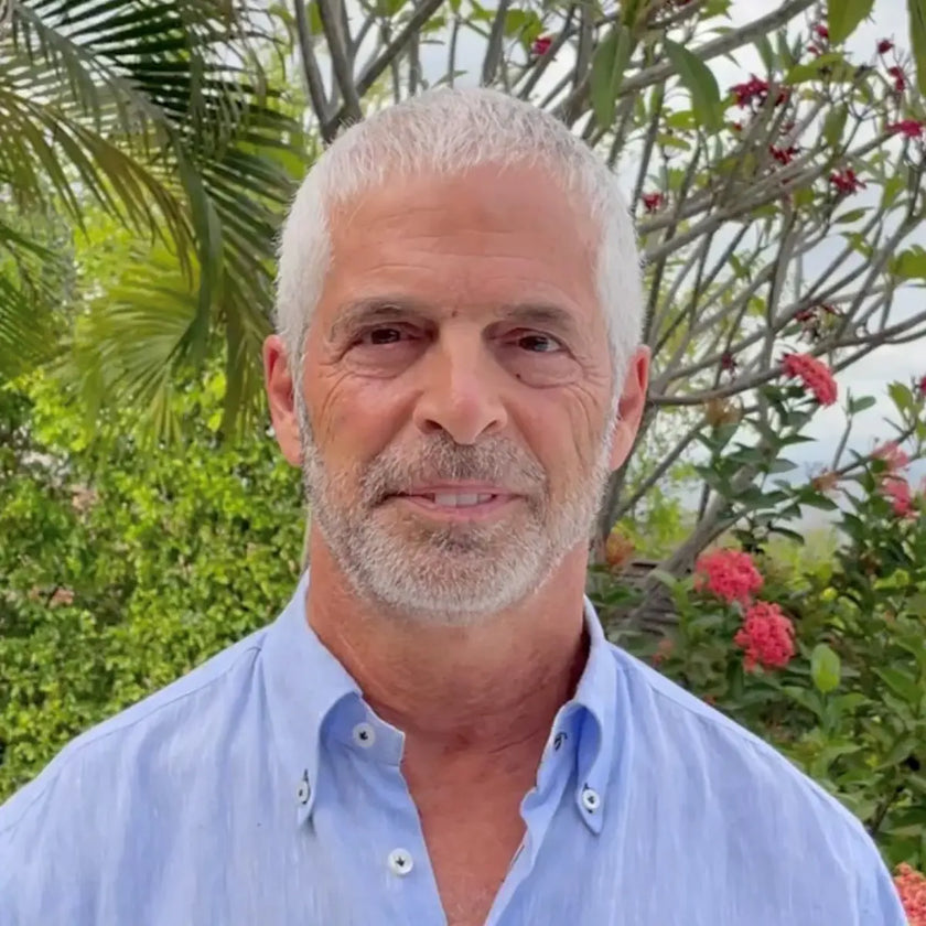Dr Tom O'Bryan wearing a light blue shirt outdoors with greenery and flowers in the background