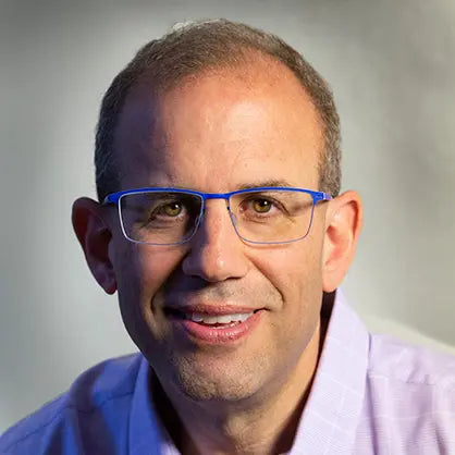 Dr Josh Helman wearing blue glasses with a blurred background